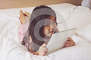 Asian little girl using tablet computer in bed.