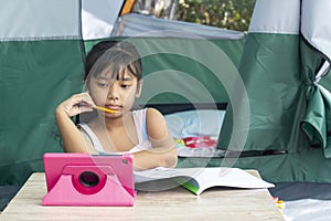 Asian little girl is using tablet to study online in tent while traveling.