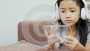 Asian little girl using white wireless headphone and clear pad for futuristic technology mobile application concept