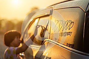 Asian little girl writing or drawing heart symbol on wet mirror of her father SUV car in morning