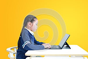 Asian little kid girl in school uniform using laptop on table isolated on yellow background, Studio shot
