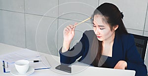 Asian long hair beautiful business woman in navy blue suit thinking about solution of her job. She sit and hold a pencil while