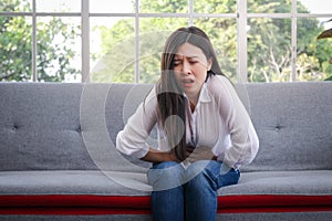 Asian long haired beautiful woman has a stomachache Sit on the sofa in the living room at home.