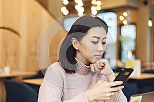 Asian lovely girl climb on the phone in a coffee shop. A pretty beautiful woman is looking for information on the Internet or