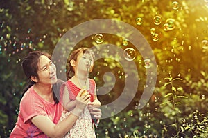 Asian lovely girl and her mother blowing soap bubbles. Family at