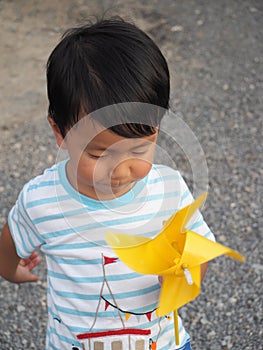 Asian lovely kid turning yellow windmill toy by hand with small stones background.