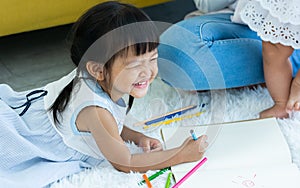 Asian lovely little daughter girl playing with fun and happiness in living room at indoor home, smiling, using color pencils to