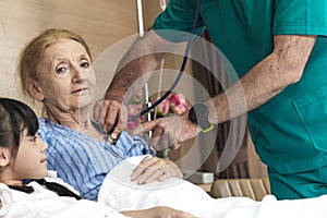 Asian lovely young girl visit and encourage grandmother when The doctor examines a elder patient on patient bed in hospital