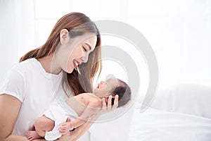 Asian loving mom carying of her newborn baby at home. Happy mum holding sleeping infant child on hands. Mother hugging her little