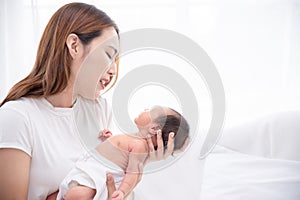 Asian loving mom carying of her newborn baby at home. Happy mum holding sleeping infant child on hands. Mother hugging her little