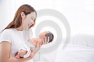 Asian loving mom carying of her newborn baby at home. Happy mum holding sleeping infant child on hands. Mother hugging her little