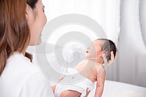 Asian loving mom carying of her newborn baby at home. Happy mum holding sleeping infant child on hands. Mother hugging her little