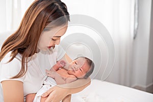 Asian loving mom carying of her newborn baby at home. Happy mum holding sleeping infant child on hands. Mother hugging her little