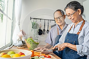 Asian loving senior elderly couple wear apron and cooking in kitchen. Attractive strong old man and woman grandparent wear