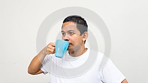 Asian Malay man sipping a drinks from blue tea cup on his hand