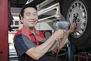 An Asian male auto technician is changing car wheel at service garage.