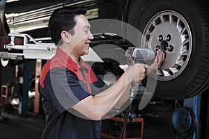 An Asian male auto technician is changing car wheel at service garage.