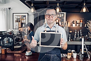 Asian male barista wear jean apron thumbs up at blank blackboard