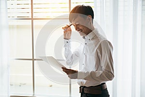 Asian male businessman reading business contract documents in private workroom.