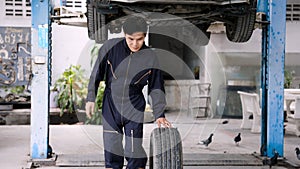 Asian male car repairman rolling a car tire. by skilled mechanics to change all 4 tires to put the car parked waiting to be