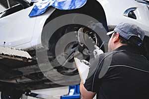 Asian male car technician car maintenance for customers according to specified vehicle maintenance checklist. Disk brake pad wear