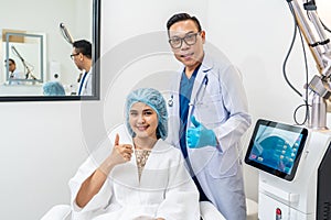 Asian male cosmetologist and young woman patient with blue cap on head in cosmetological clinic