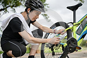 An Asian male cyclist fixes his bike chain on the street after riding on country roads