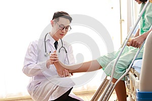 Asian male doctor examining the ankle of a female patient