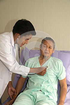 Asian male doctor examining elderly male Asian patient in hospital which was lying on the bed.