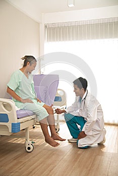 An Asian male doctor examining the reactions of an Asian male patient. neurologist using a knee hammer which is a medical device.