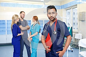 Asian male doctor in front of team, looking at camera with medical team in background. Multiracial team of young doctors