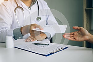 Asian male doctor talking in clinic room and handing a prescription to the patient