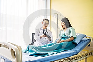 Asian male doctor talking to asian female patient in bed, while explaining exam results in computer to patient at medical