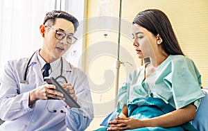 Asian male doctor talking to asian female patient in bed, while explaining exam results in computer to patient at medical