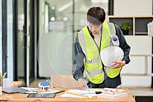 An Asian male engineer or architect is checking the building\'s plan design on the blueprint