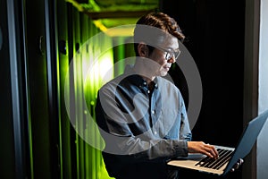 Asian male engineer using laptop in computer server room