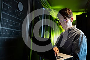 Asian male engineer using laptop in computer server room