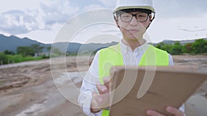 Asian male engineer wear safety vest protection helmet looking at digital tablet on outdoor site, specialist expert knowledge, con