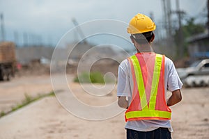 Asian male engineering worker wearing hard hat and protective vest standing back and look forward at construction site