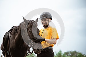 Asian male equestrian in equestrian equipment stroking horse