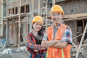 Asian male and female contractors standing with crossed hands smiling at the camera wearing safety helmets