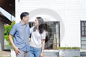 Asian male and female couples stand, hug, and smile happily in front of the new house.