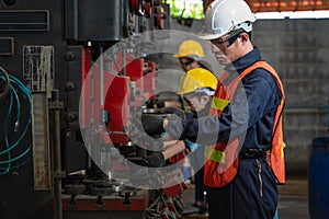 Asian male and female manufacturing workers operating steel drilling machine together in line of metal work production factory