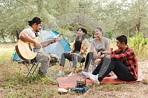 Asian male and female tourists are tenting and partying, chatting, singing and playing guitar in the forest