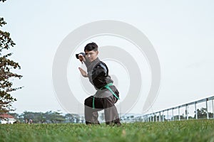 Asian male fighters wearing pencak silat uniforms perform low stance movements