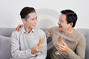 Asian male friends and sitting on the sofa and drinking champange, discussing something and laughing