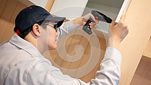 Asian male furniture assembler using electric drill screwdriver