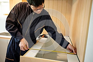 Asian male furniture assembler using tape measure