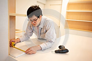 Asian male furniture assembler using tape measure