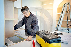 Asian male furniture assembler using tape measure